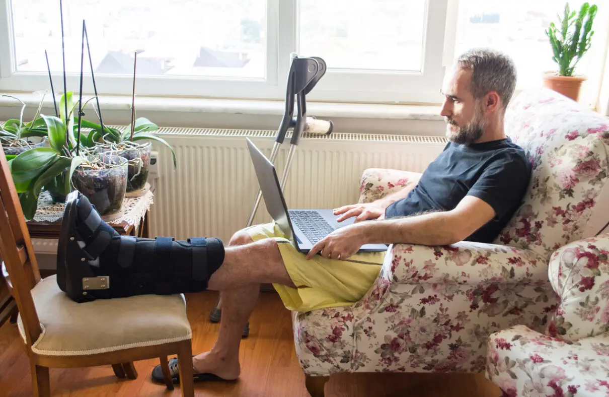 A man with a broken leg using his laptop while recovering at home