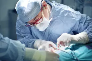 A surgeon with glasses operating on a patient