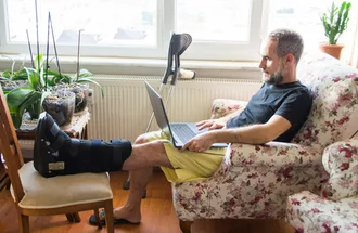A man with a broken leg using his laptop while recovering at home